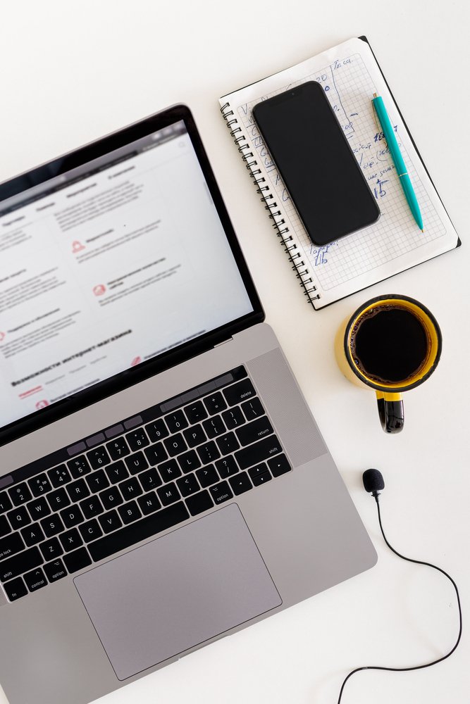Online education or training course concept Laptop with microphone, smartphon, notebook and cup of coffee on white table top view